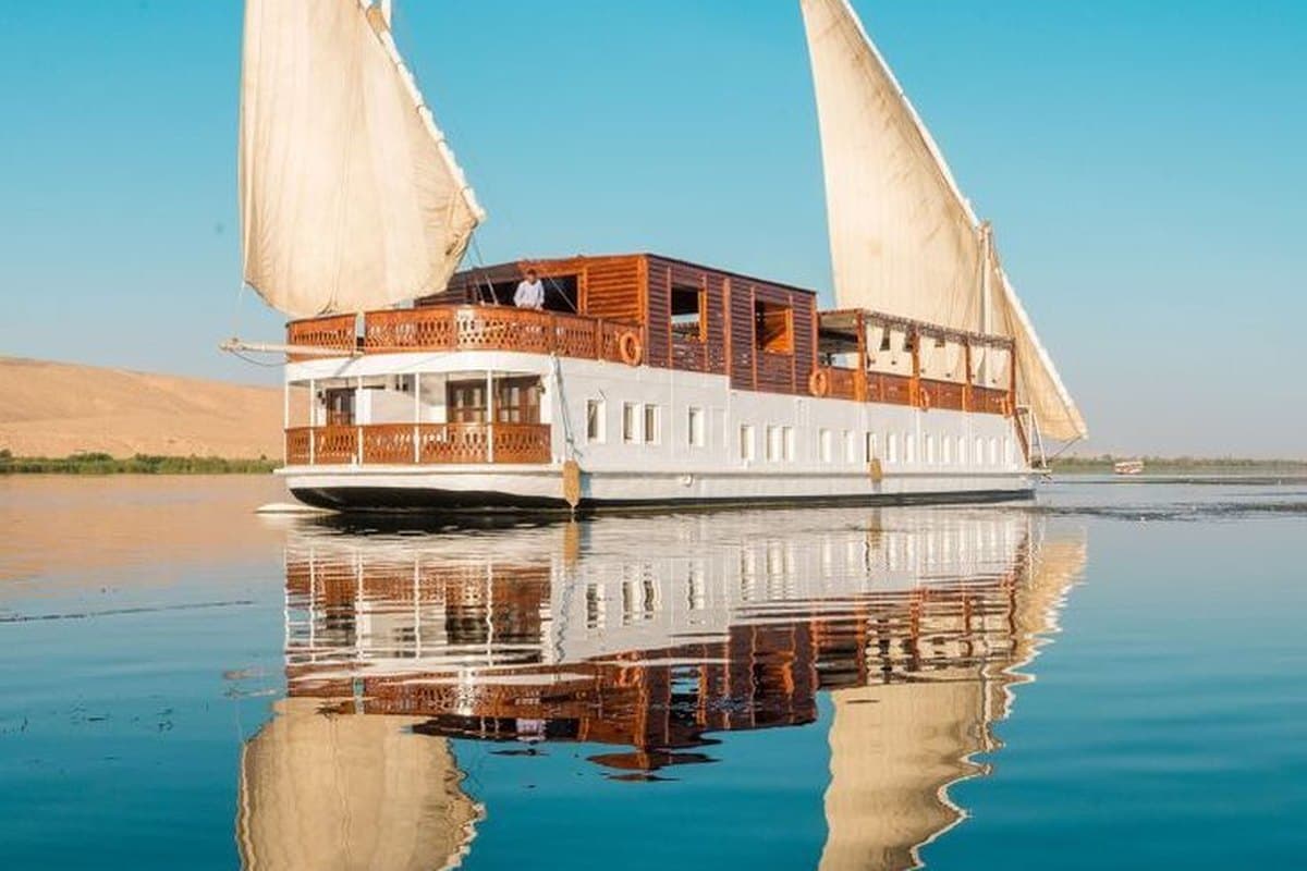 A dahabiya moored on a still stretch of the Nile, its sails and hull mirrored in the water